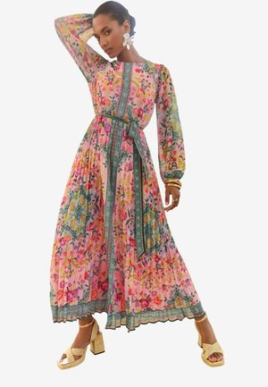 Long, flowing dress in pink floral print with long sleeves, a defined waist, and a green patterned trim. Paired with woven gold platform sandals.