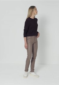 Top marrón de manga larga combinado con pantalones beige ajustados y deportivas blancas. El top presenta botones en las mangas. Estilo simple y moderno.