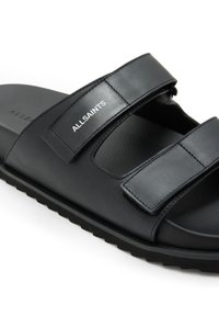 Sandalia deslizante de cuero negro con correas de Velcro. Presenta una plantilla texturizada y una suela de goma gruesa. Logo de "ALLSAINTS" en la correa.