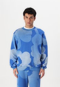 Blå sweatshirts med stora ljusblå blommönster, rund halsringning och ribbad mudd. Matchas med matchande blå byxor för en koordinerad look.