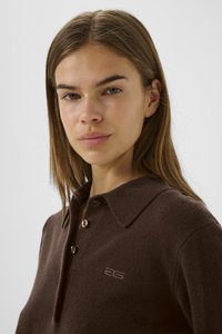 Bruine gebreide polo met een kraag, voorzien van drie knopen en een klein logo. Soepele textuur, nauwsluitende pasvorm.