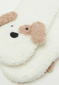 Calze bianche pelose con un design a forma di volto di cane, con orecchie marroni e occhi ricamati neri, realizzate in un morbido tessuto testurizzato.