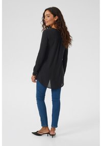 Black long-sleeve shirt with a textured fabric, featuring a curved hem, paired with blue jeans and black pointed shoes.