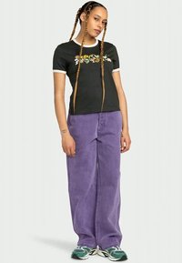 Black t-shirt with white trim and floral embroidery, paired with high-waisted, loose purple jeans and green sneakers.