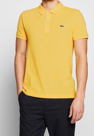 Yellow polo shirt made of textured fabric, featuring a collar and three-button placket, with a small green logo on the chest.