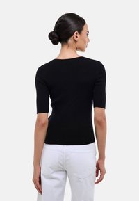 Haut noir à manches courtes en côte avec un design ajusté. Le dos présente une encolure arrondie. Associé à un pantalon blanc taille haute.