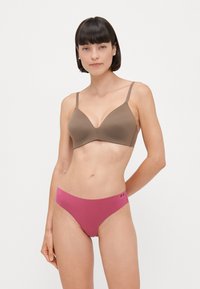 Seno reggiseno wireless marrone con una texture liscia e morbida e una scollatura profonda, abbinato a mutandine hipster rosa con un dettaglio del logo.