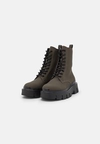 Bottes de cheville vert olive avec des semelles en caoutchouc noir épaisses et des lacets noirs. Présentent une finition lisse et des détails de couture renforcés.