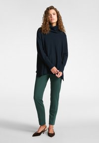 Marineblauw coltrui met lange mouwen, gecombineerd met groene taps toelopende broek en bruine hakken. Glad breiwerk met zijsplitten.