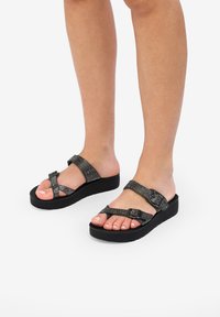 Sandalias de plataforma negras con tiras texturizadas que presentan acentos de rhinestones, cierre de hebilla y una suela acolchada para mayor comodidad.