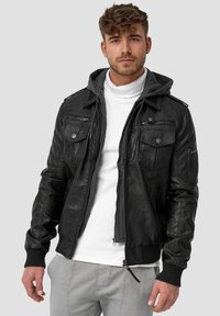 Black leather jacket with a hood, featuring zippered pockets, ribbed cuffs, and a smooth texture. Styled over a white turtleneck.