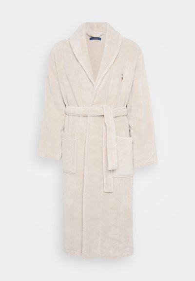 Μπεζ, αφράτη ρόμπα μπάνιου με γιακά τύπου σαλονιού, ζώνη και δύο μπροστινές τσέπες. Πληροφορείται από ένα μικρό λογότυπο στο στήθος. Μαλακό, υφασμάτινο υλικό.