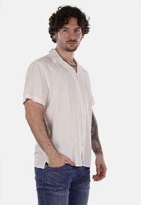 Camicia bianca a maniche corte, con bottoni, realizzata in tessuto leggero, dotata di colletto e vestibilità rilassata, abbinata a jeans in denim.