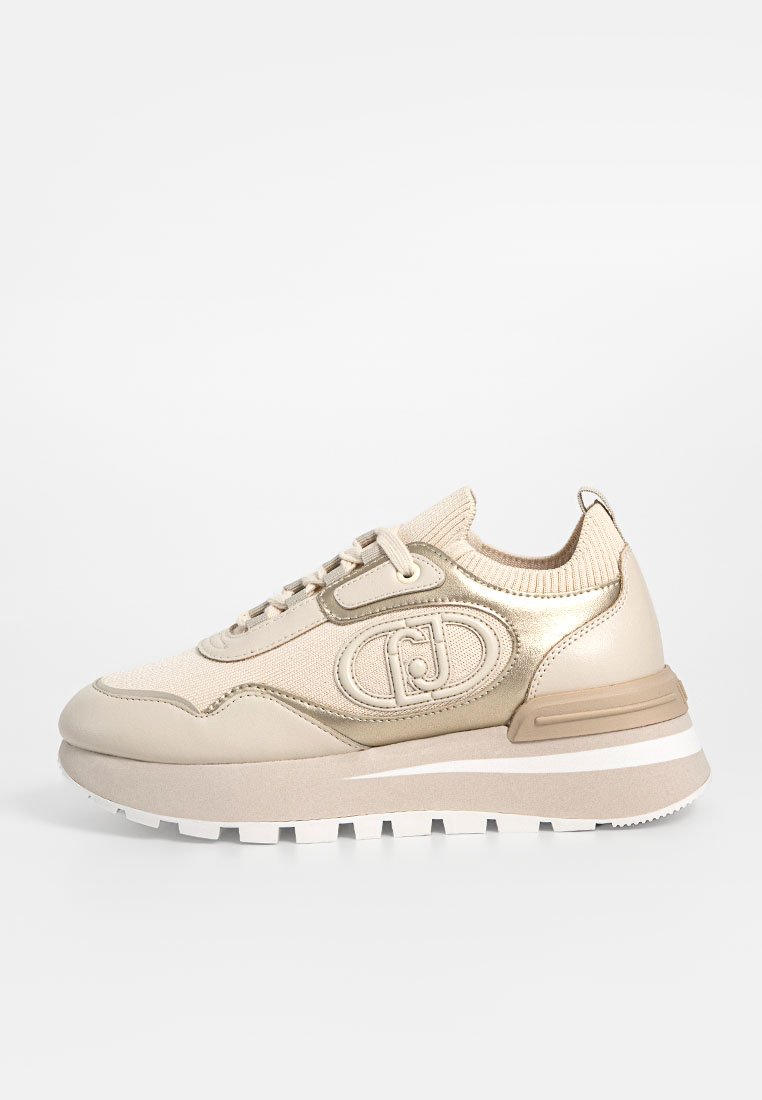 Sneaker sportivo beige caratterizzato da materiali in mesh e sintetici, punta rotonda, suola spessa e dettaglio del logo sul lato. Tallone rinforzato.