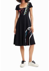Černé šaty s krátkým rukávem, čtvercovým výstřihem, s barevnými abstraktními vzory v červené, modré a bílé barvě. Doplněné o bílé tenisky.