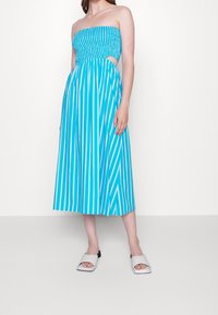 Blue and white striped strapless dress with a smocked bodice, side cutouts, and a flowy midi-length skirt. Worn with white slide sandals.