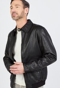 Zwart leren jack met een kraag, ritssluiting aan de voorkant en geribbelde zoom. Gladde textuur met een subtiele glans en gedetailleerde stiksels.