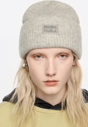 Szary dzianinowy beanie o prążkowanej fakturze z prostokątną naszywką logo. Model nosi żółtą bluzę z czarnym kapturem pod spodem.