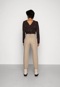 Blusa de manga larga con un estampado de leopardo negro y marrón, diseño en V en la parte posterior, combinada con pantalones de tiro alto beige y botas de tobillo.