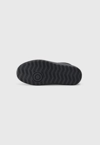 Fekete sneaker talp zigzag mintázattal és középen egy kör alakú díszítéssel. Az anyag gumi jellegű, a tapadás és tartósság érdekében.