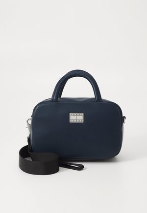 Bolso de mano de cuero sintético azul marino con forma rectangular, doble asa, correa negra desmontable y placa del logo de la marca en plateado.