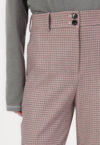 Calças xadrez com um padrão em vermelho, preto e branco, com uma textura suave e dois botões pretos na cintura.