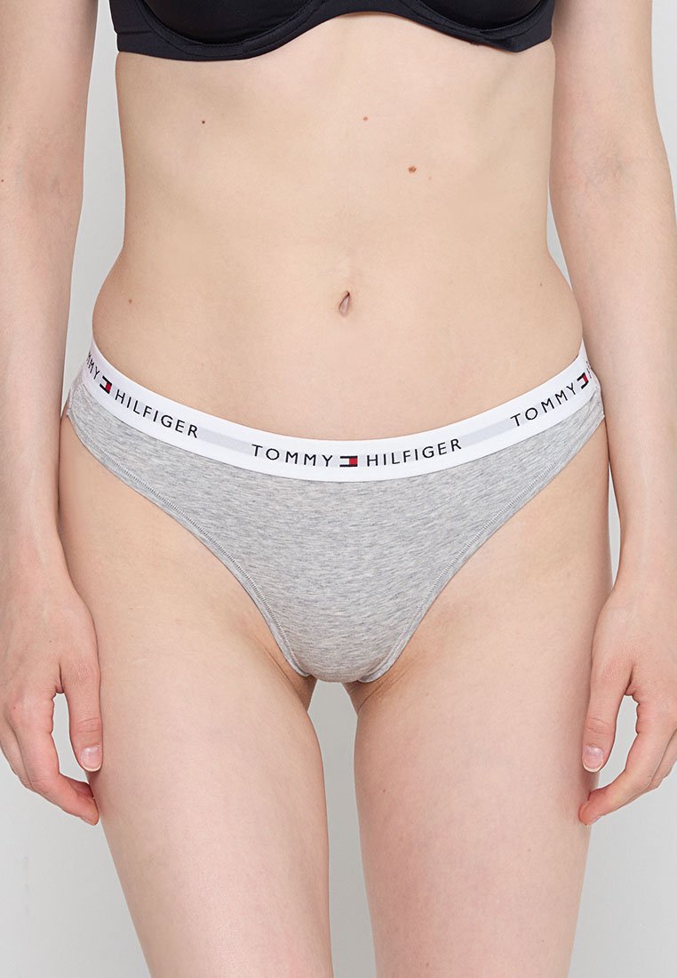 Tanga de algodón gris con una cinturilla blanca que presenta el logotipo "TOMMY HILFIGER". El diseño incluye una textura suave y un estilo minimalista.
