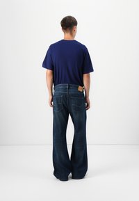 Jeans de gran tamaño en azul oscuro con piernas anchas, combinados con una camiseta ajustada también en azul oscuro. Costuras y bolsillos visibles en los jeans.