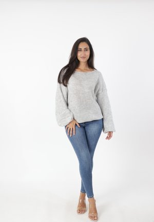 Suéter de punto gris claro con mangas anchas, combinado con jeans ajustados azules y tacones transparentes. El suéter presenta un escote amplio y un acabado texturizado.