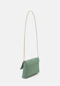 Small rectangular green handbag with flap closure and long thin gold chain strap hanging against a white background.