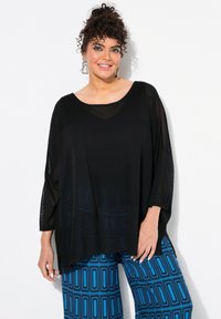 Schwarzes, übergroßes Oberteil mit strukturiertem Muster, das gut zu leuchtend blauen, gemusterten weiten Hosen mit rechteckigen Designs passt.