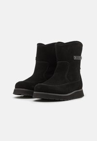 Stivaletti alla caviglia in suede nero con punta arrotondata, cuciture sottili e suola piatta in gomma. Presenta un piccolo accento metallico con il marchio.