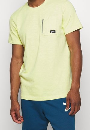 Kurzärmliges, hellgelbes Nike-T-Shirt mit einer vorderen Tasche mit Reißverschluss. Der Stoff hat eine strukturierte Oberfläche.