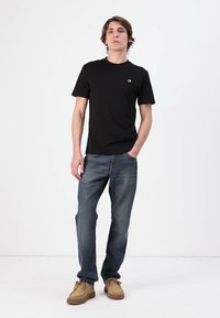 Svart kortärmad T-shirt med rund hals; kombinerad med blå denimjeans och ljusbruna skor med en texturerad sula. Enkelt utförande, inga mönster.