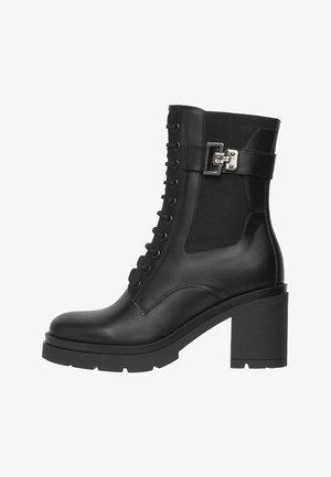 Black leather ankle boot with block heel, lug sole, lace-up front, elastic side panel, and decorative silver buckle strap.