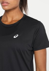 Camiseta deportiva negra con cuello redondo, mangas cortas y tejido texturizado. Presenta un pequeño logo blanco en el pecho.
