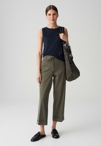 Navy sleeveless top, olive green high-waisted pants, black slip-on shoes, braided bag with striped accent. Casual outfit with loose fit.