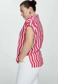 Short-sleeved blouse featuring wavy pink and white stripes. Made of light fabric with a relaxed fit, paired with white pants.