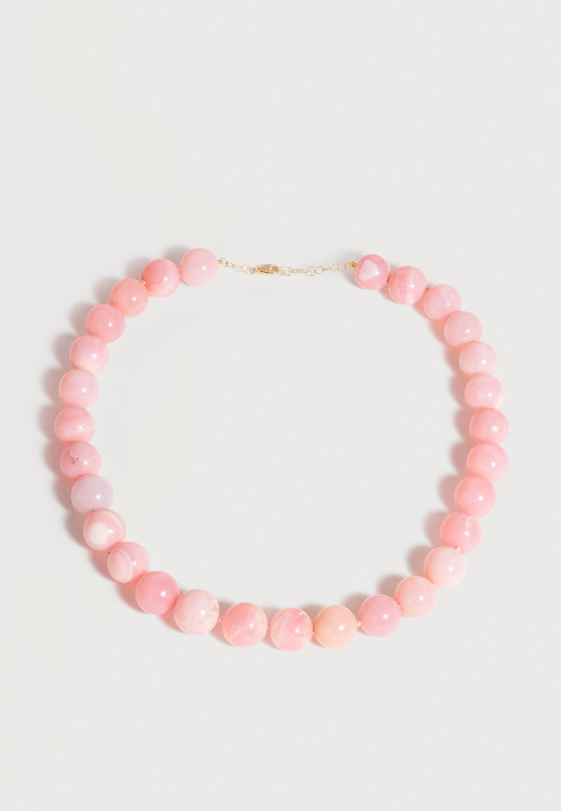 Collier de perles roses rondes polies avec fermoir en or, disposé en cercle sur fond blanc.