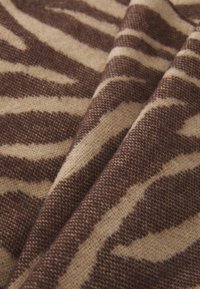 Brun og beige mønstret stof med en fuzzy tekstur, der har et zebra-stribe design i kontrasterende nuancer. Nærbillede af folder.