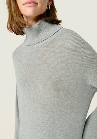 Maglione a collo alto di colore grigio chiaro con texture a costine, caratterizzato da una vestibilità aderente e maniche lunghe, realizzato in morbido materiale lavorato a maglia.