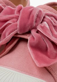 Sneaker rosa con un morbido fiocco in velluto, tomaia rosa texturizzata e suola in gomma bianca con dettagli rigati.