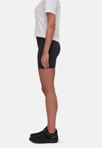Shorts atletici neri con vestibilità aderente e materiale elasticizzato, abbinati a una maglietta bianca a maniche corte e scarpe sportive nere.