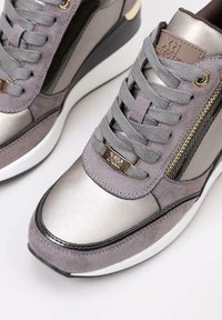 Zapatillas metálicas de color gris que presentan una combinación de texturas lisas y de ante, cordones planos, cremallera lateral y accesorios en dorado.