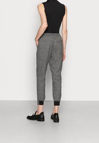 Grijs geblokte broeken met taps toelopende benen, elastische tailleband en zwarte omgeslagen zomen. Het model draagt zwarte schoenen en toont een minimalistisch ontwerp.