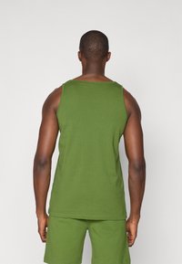 Grønn tank topp laget av bomull, med en klassisk fasong og en glatt tekstur, kombinert med matchende shorts, sett bakfra.