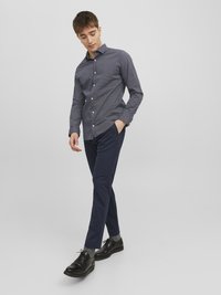 Košulja s mornarskim uzorkom dugih rukava, uparena sa slim-fit mornarskim hlačama i crnim cipelama na vezanje. Glatka tkanina, strukturirani kroj, minimalne detalje.
