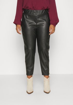 Czarne spodnie ze sztucznej skóry z nogawkami zwężanymi ku dołowi, elastyczną talią i zamkami błyskawicznymi przy mankietach, w połączeniu z beżowymi botkami za kostkę.