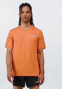 Camiseta deportiva naranja de manga corta y cuello redondo; presenta el logo de TERREX en blanco, fabricada con un material ligero y transpirable.