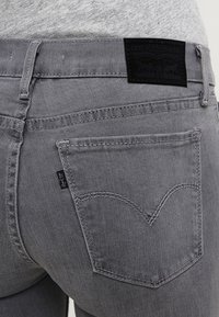 Vaqueros de mezclilla gris con un acabado texturizado, con una etiqueta negra en la cintura y costuras clásicas en los bolsillos traseros con un diseño curvado.